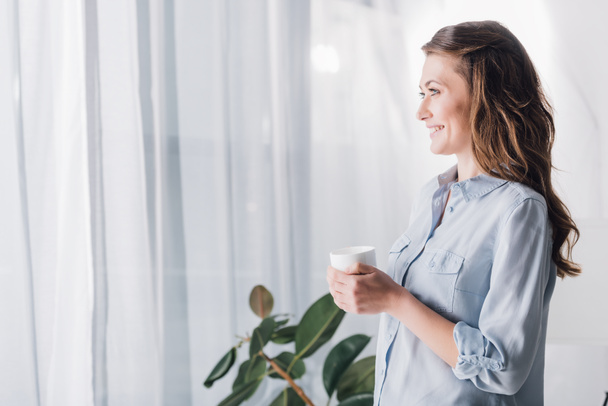 happy adult woman holding cup of hot coffee and looking away - Foto, Imagem