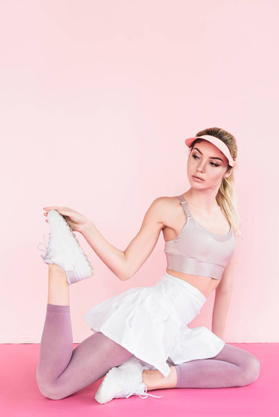 young stylish female athlete in visor hat exercising on pink - Foto, afbeelding