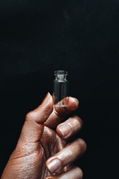 γυναικείο χέρι κρατώντας το μικρό μπουκάλι καθαρό σε μαύρο φόντο - Φωτογραφία, εικόνα