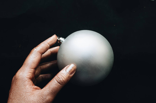 female hand holding grey Christmas ball on black background  - 写真・画像