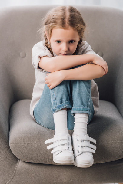 lonely little child sitting in armchair and looking at camera - Photo, image