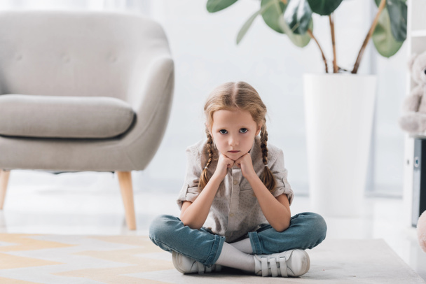 lonely depressed little child sitting on floor of empty room and looking at camera - Photo, Image