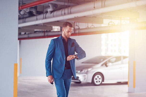 Be in time. Serious elegant handsome businessman standing in the parking lot and looking at his wrist watch on his way to work - Photo, image