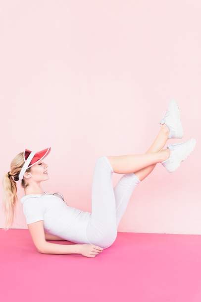 side view of happy female athlete in visor hat exercising on pink - Foto, immagini