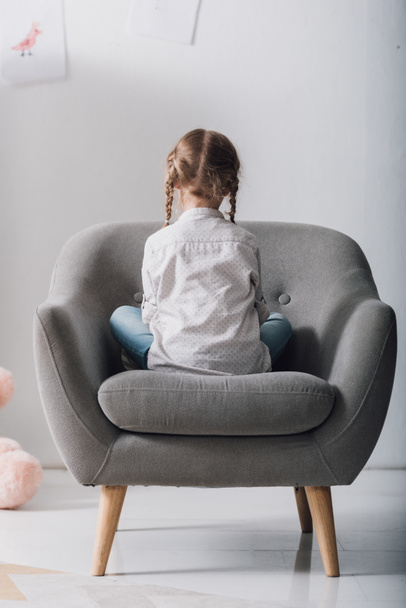 rear view of lonely little child sitting in armchair in front of white wall - Fotografie, Obrázek