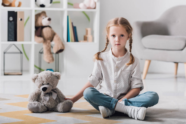 lonely little child sitting on floor with teddy bear and looking at camera - Fotografie, Obrázek