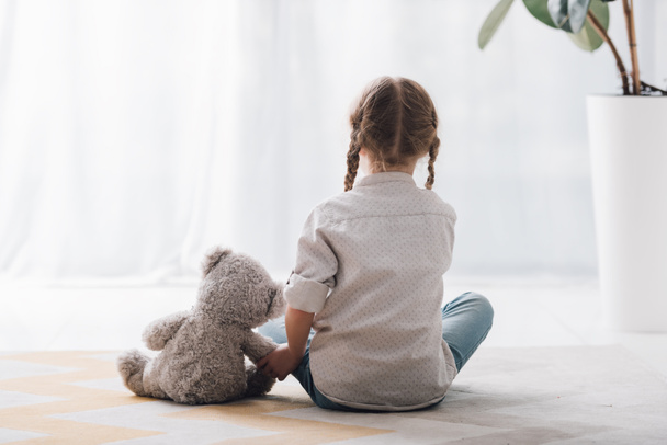 rear view of little child sitting on floor with her teddy bear toy - Photo, Image