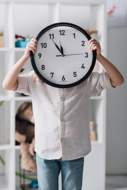 little child covering face with big clock - Φωτογραφία, εικόνα