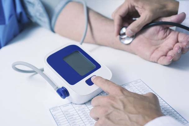 крупним планом кавказький лікар, в білій шубці, вимірюючи кров'яний тиск старшого кавказького пацієнта зі сфінгометром
 - Фото, зображення