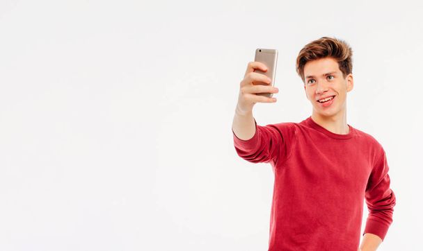 Attractive young man teenager makes a selfie with smartphone on white background, banner - Photo, Image