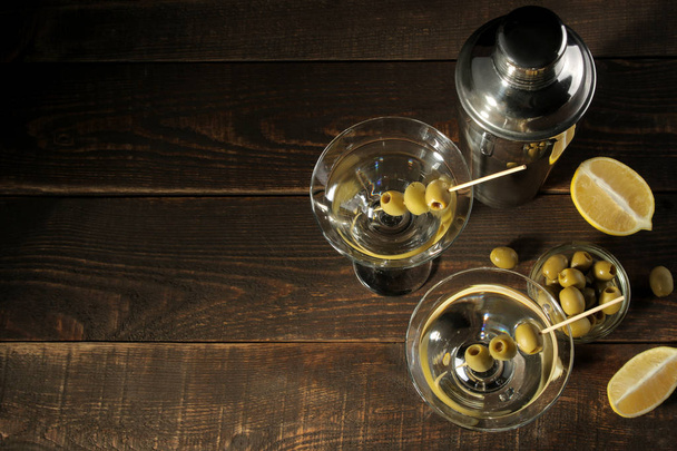 Martini v skleněné sklenici s zelenými olivami na jehle na hnědý dřevěný stůl. koktejly. Bar - Fotografie, Obrázek