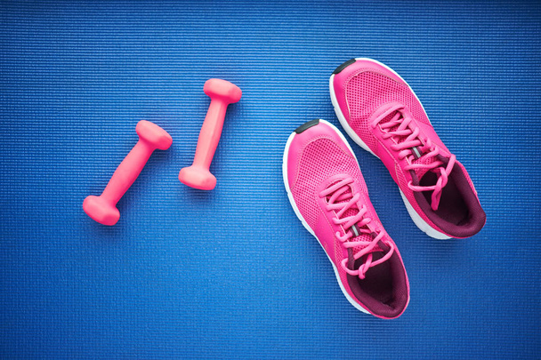 Set van sneakers en roze dumbeells op de blauwe achtergrond, bovenaanzicht - Foto, afbeelding