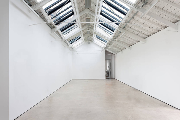 Una vista de un interior pintado de blanco de una habitación vacía o una galería de arte con una claraboya de iluminación y pisos de hormigón
 - Foto, imagen