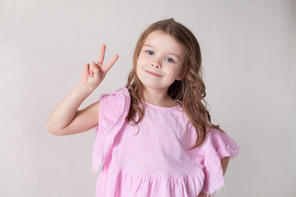 ένα μικρό κορίτσι σε ένα ροζ φόρεμα δείχνει δύο δάχτυλα - Φωτογραφία, εικόνα