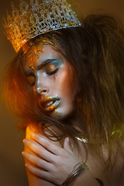 Striking girl with creative make up with feathering and smudges of gold on dark background with lighting - Foto, Bild