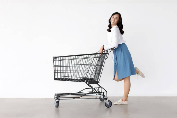 白い背景の上のショッピングカートとアクションを買い物で幸せなアジア女性.   - 写真・画像