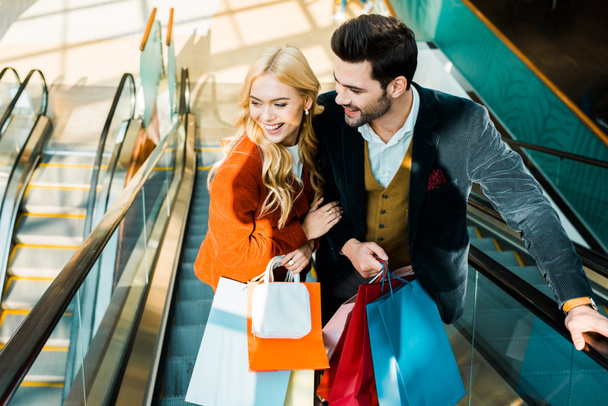 elegant smiling couple with shopping bags standing on escalator - Φωτογραφία, εικόνα