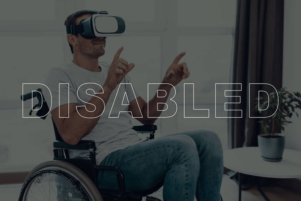 Disabled Man in a Wheelchair. Man Wearing a Virtual Reality Glasses. Man is Gesticulating of Hands. Man is Smiling. Adult Brunette Man. Man is Located in the Living Room. Virtual Technologies. - Photo, image