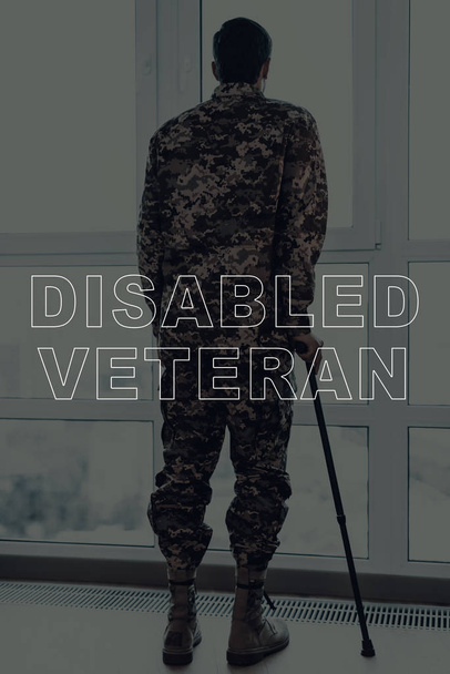 Military Veteran. Man Standing in Front of Window. Large Panoramic Window. Man with Crutch. Man is Soldier. Soldier in Military Uniform. Man Looking into Window. Man Located in the Living Room. - Foto, imagen