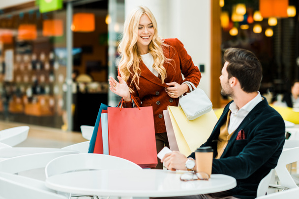 attrayant femme avec des sacs à provisions saluant petit ami dans le café dans le centre commercial
 - Photo, image