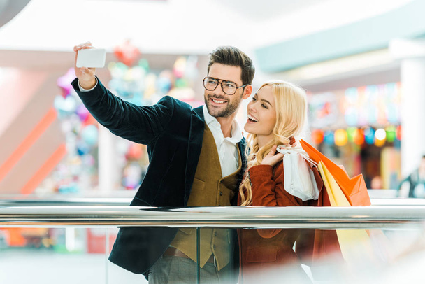 fiatal izgatott pár bevásárló szatyrok selfie véve a smartphone  - Fotó, kép