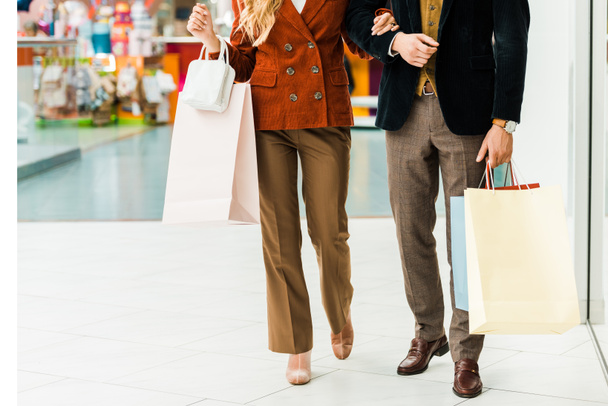 vista recortada de pareja joven con bolsas de compras caminando en el centro comercial
 - Foto, Imagen