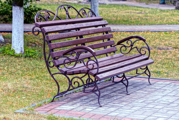 коричневая скамейка стоит на тротуаре в зеленой траве
 - Фото, изображение