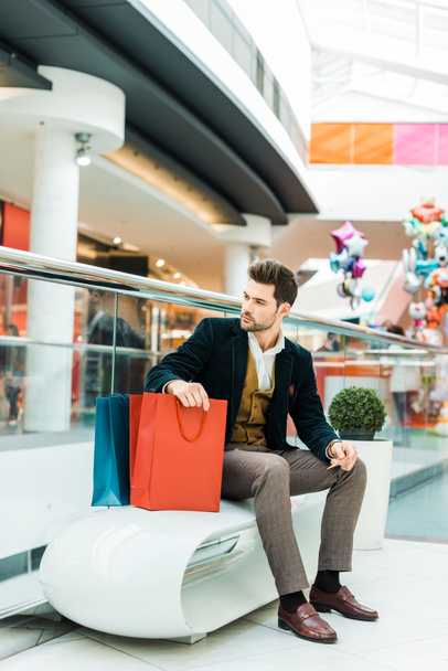 fashionable man holding credit card and sitting with bags in shopping center - Φωτογραφία, εικόνα
