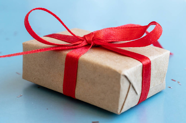 A gift box, beautifully wrapped with kraft paper and red ribbon and large bow on blue background. - Zdjęcie, obraz