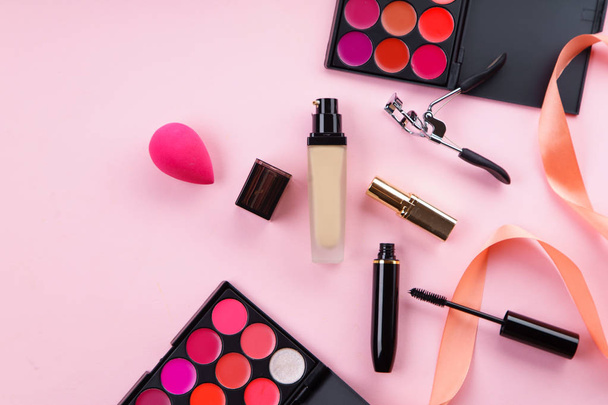 lipstick palettes and foundation with mascara and eyelash curler on pink background. Makeup artist kit concept - Foto, imagen