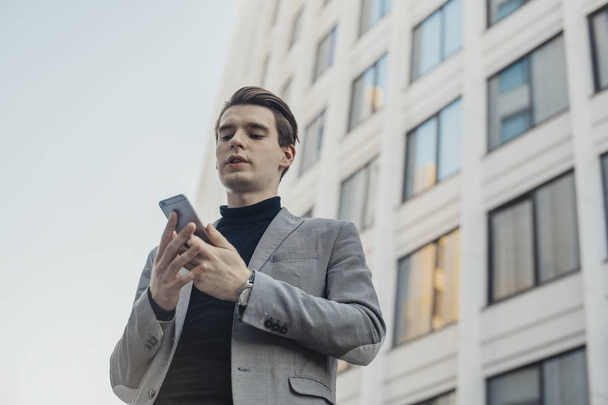 Close up of young businessman talking by mobile phone next to business center. - Photo, Image