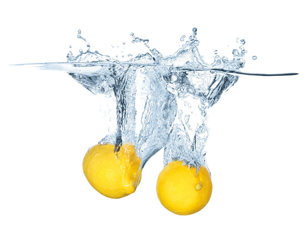 Due limoni maturi cadono in acqua con schizzi isolati sul bianco. Contesto rinfrescante, concetto e idea di cibo sano
. - Foto, immagini