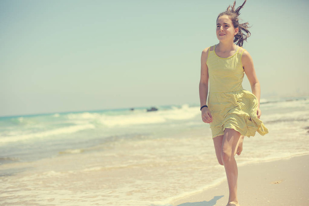 12 years old girl teen girl in yellow dress walking on seaside. Summer vacation - Photo, Image