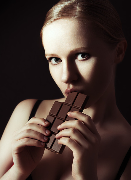セクシーな美しい若い女性は、暗いチョコレートを食べる - 写真・画像