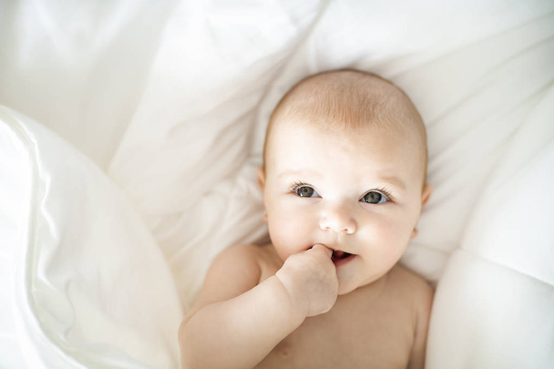 Um bebê bonito menina em uma cama branca em casa
 - Foto, Imagem