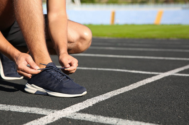 Sporty man tying shoelaces before running at stadium on sunny morning - Φωτογραφία, εικόνα