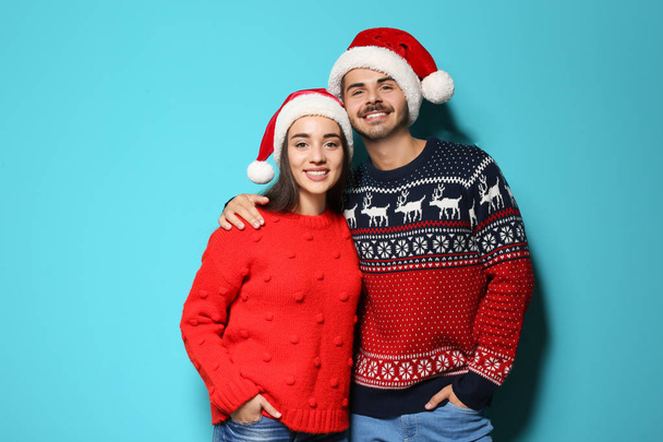 Young couple in warm sweaters and Christmas hats on color background - Foto, Bild