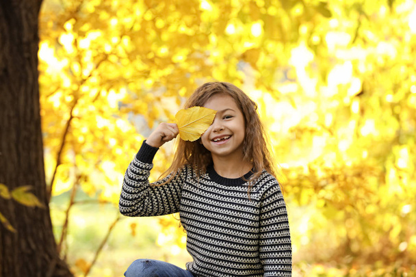 Cute little girl with leaf in park. Autumn walk - 写真・画像