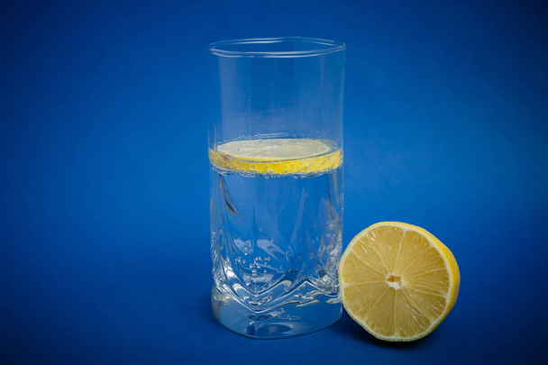 lemon with water in a glass on a blue background - Fotoğraf, Görsel
