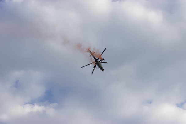 Combat helicopter with red smoke on blue sky with white clouds. View from the bottom.  - Photo, Image