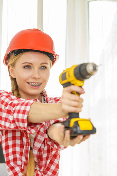 Een vrouw die een helm draagt met een boor. Meisje dat werkt bij flat remodeling. Bouw, reparatie en renovatie. - Foto, afbeelding
