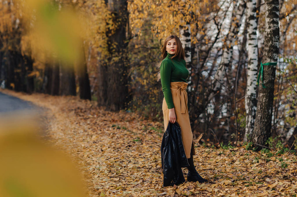 άνετο και κομψό νεαρό κορίτσι με τα πόδια στο φθινόπωρο πολύχρωμο πάρκο μόνος - Φωτογραφία, εικόνα