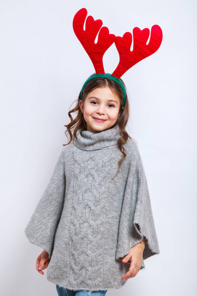 Happy little smiling girl showing product. Christmas concept. Smiling funny girl in deer horns in studio. - Foto, Bild