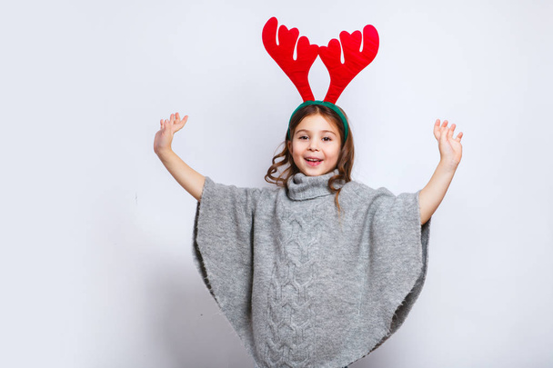 Happy little smiling girl showing product. Christmas concept. Smiling funny girl in deer horns in studio. - Foto, imagen