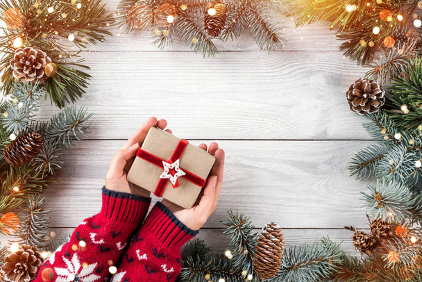 Nainen kädet tilalla joululahja laatikko valkoinen puinen tausta Fir oksat, mänty käpyjä. Joulua ja onnellista uutta vuotta teema, bokeh, kipinä, hehkuva. Tasainen, ylhäältä
 - Valokuva, kuva