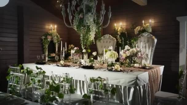 ένα τραπέζι που με μαύρα βέλη με φαγητό, ποτήρια κρασιού, βάζα λουλουδιών, κηροπήγια με λαμπάδες, πίσω από το οποίο ξεχωρίζει δύο θρόνους - Πλάνα, βίντεο