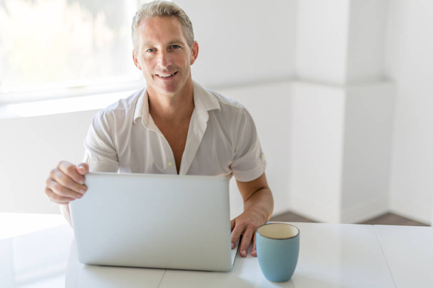 Mature Man Using Laptop On Desk At Home - Foto, afbeelding