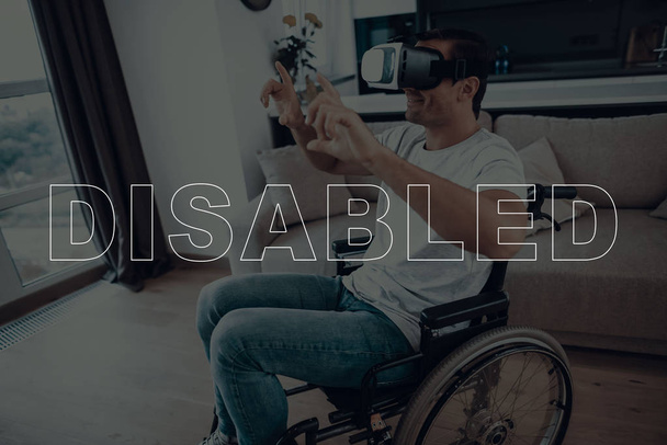 Disabled Man in a Wheelchair. Man Wearing a Virtual Reality Glasses. Man Showing Sign of Photo Camera. Adult Brunette Man. Man Smiling. Man is Located in the Living Room. Virtual Technologies. - Foto, Imagen