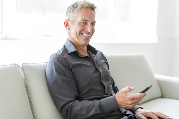 Портрет зрілого чоловіка, що розслабляється вдома в дивані і мобільному телефоні
 - Фото, зображення