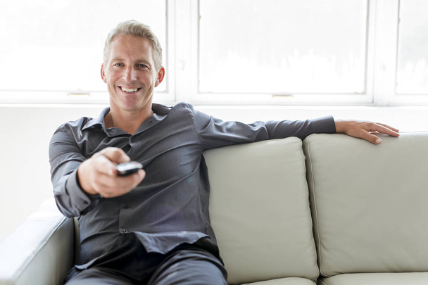 Portrait of single 40s man sitting in sofa tv remote - Fotoğraf, Görsel